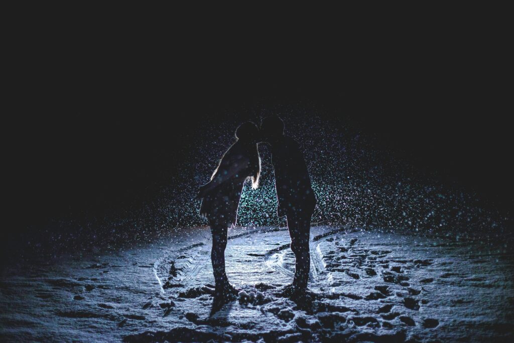 A romantic winter scene depicting a couple kissing under falling snow, creating a beautiful silhouette.
